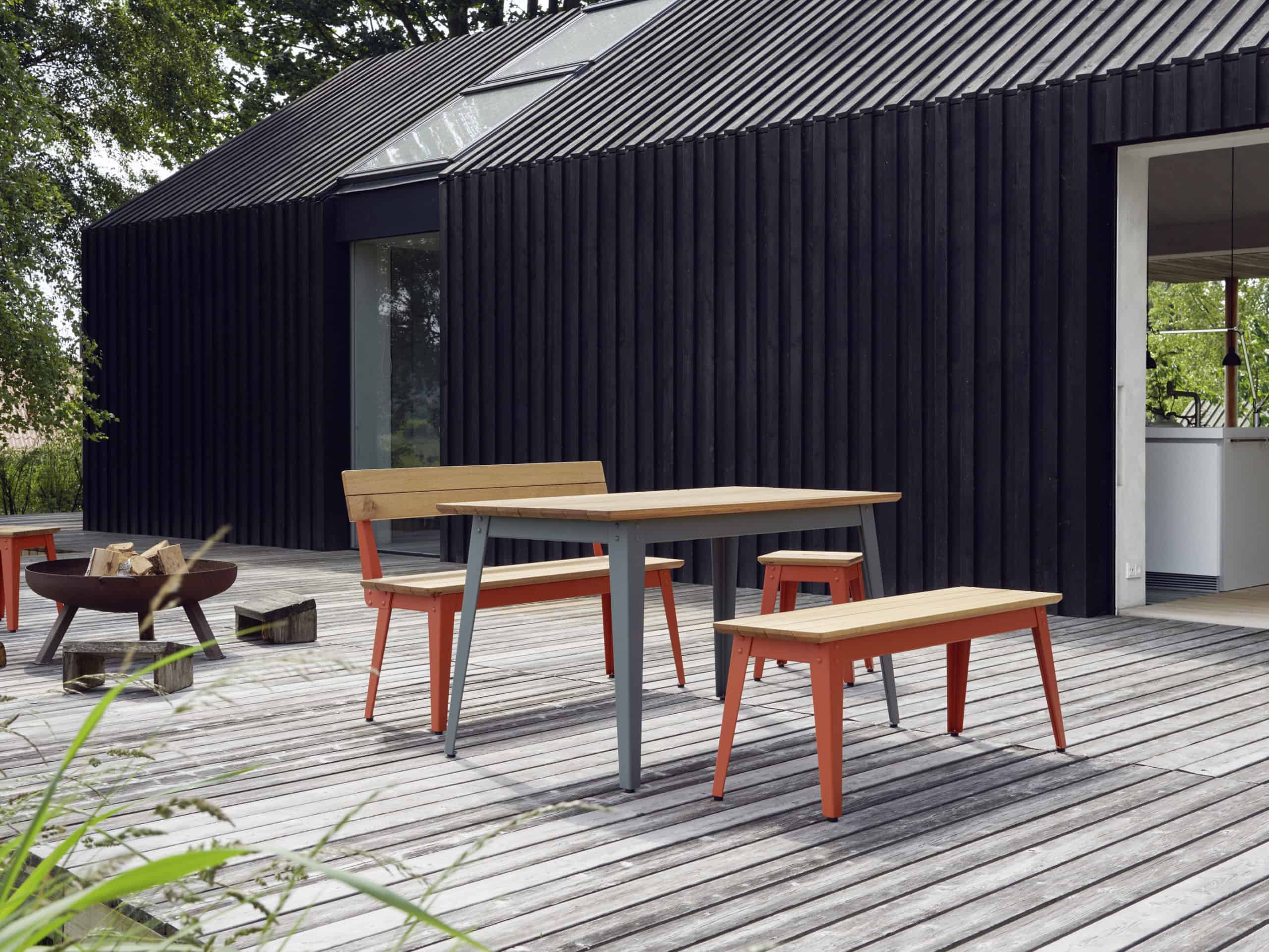 Outdoor-Tisch mit Outdoor-Hockern und Outdoor-Bänke aus Holz von Jan Cray auf einer Holzterrasse vor einer schwarzen Holzfassade.