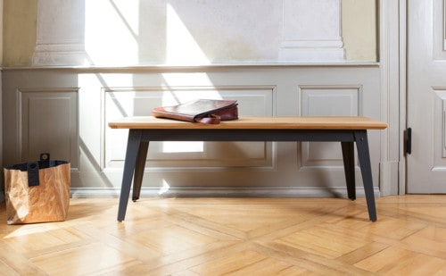 Bank mit einer Sitzfläche aus Eichenholz und einem dunkelgrauem Metallgestell. Das Möbelstück steht vor einer hellen Holzkasettenwand auf Eichenparkett.