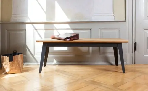 Bank mit einer Sitzfläche aus Eichenholz und einem dunkelgrauem Metallgestell. Das Möbelstück steht vor einer hellen Holzkasettenwand auf Eichenparkett.