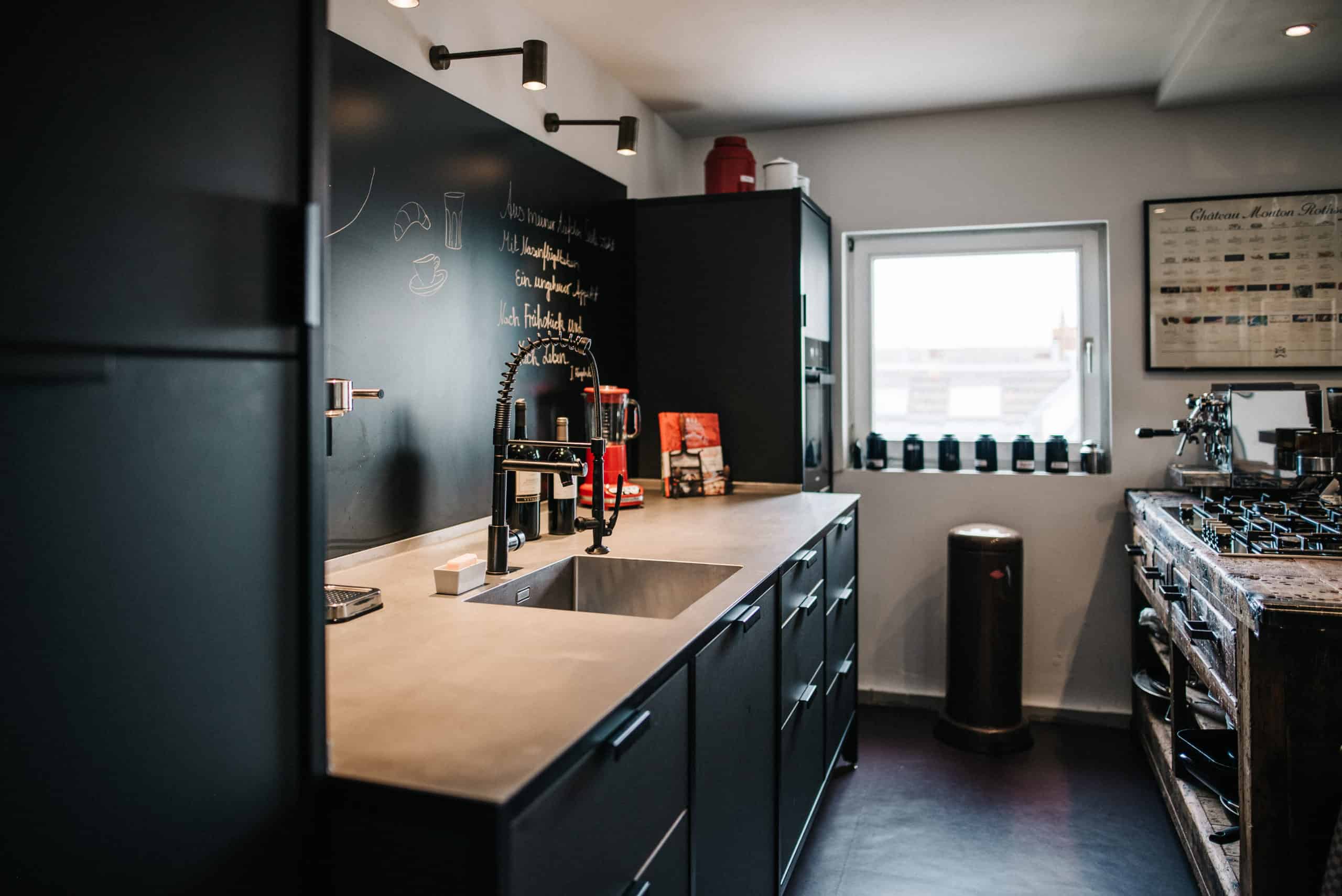 Kochbereich einer Küche im urbanen Vintage-Look. Eine schwarze Küchenzeile, Vintageobjekte und kleine, rote Farbakzente verleihen dem Ganzen einen französischen Touch.