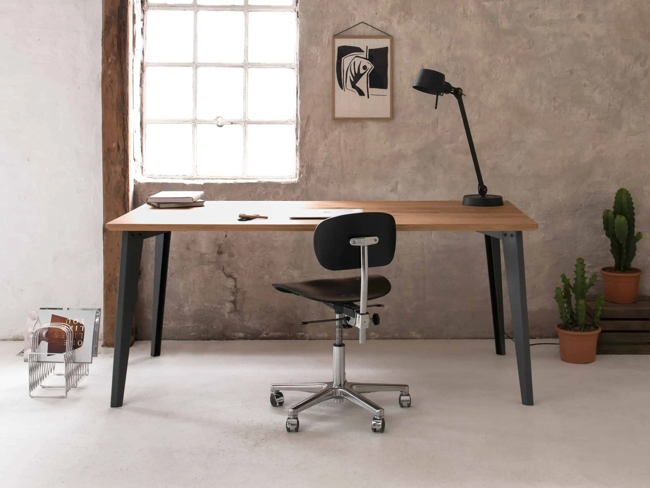Büro mit Industriecharakter: Ein Schreibtisch mit dunkelgrauem Metallgestell steht vor einer grob verputzter Wand.
